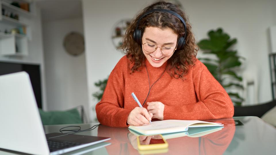 Eine Studentin in einem roten Pullover schreibt in ein Buch